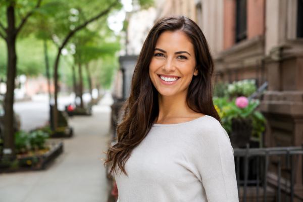 Happy adult woman smiling outdoors after Invisalign treatment with healthy straight teeth